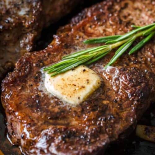 A juicy steak topped with a melted pat of butter and a sprig of rosemary, with visible seasoning and seared edges—an irresistible treat for fans of classic steakhouse flavors and steak recipes.
