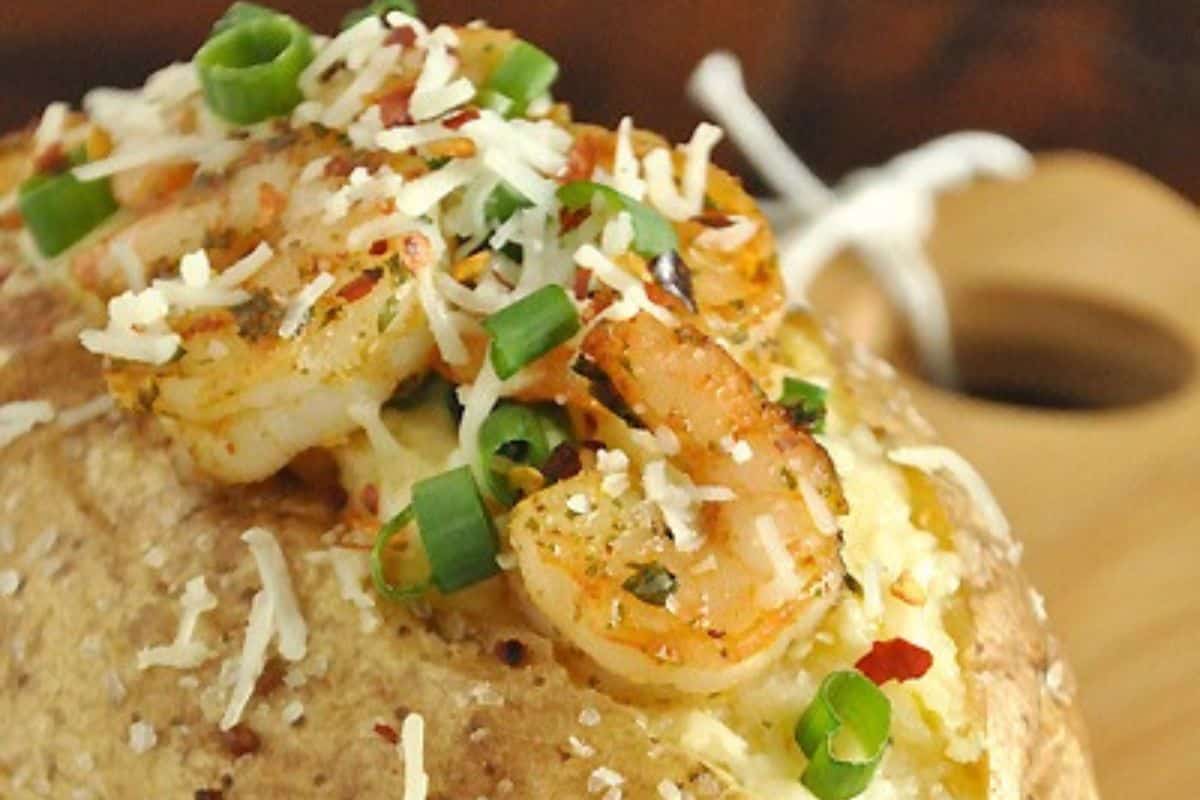 A creative baked potato topped with shrimp, shredded cheese, chopped green onions, and seasonings—perfect for those seeking unique baked potato ideas.