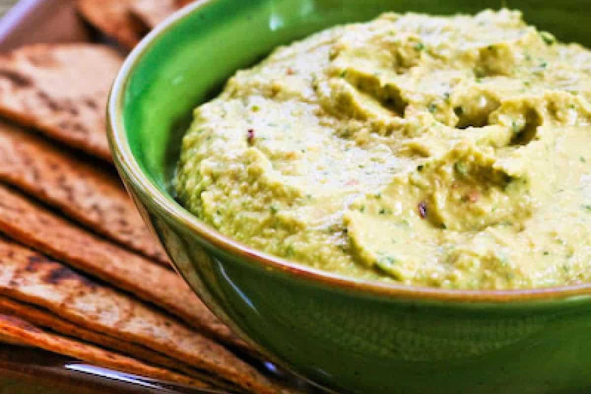 A green bowl filled with classic hummus, placed next to several pieces of flatbread or pita chips—perfect for enjoying delicious twists on your favorite hummus recipes.
