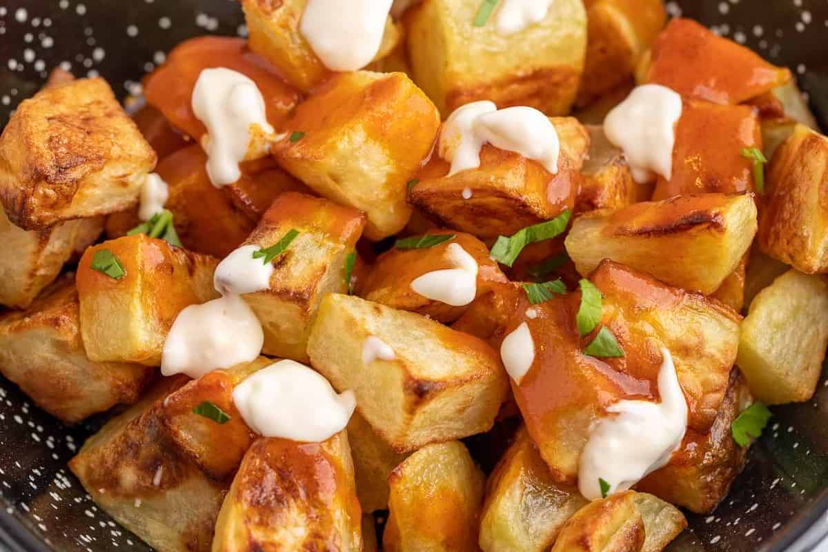A close-up of crispy roasted potato cubes topped with orange and white sauces, garnished with small green herb pieces—perfect for those seeking cold appetizer ideas.