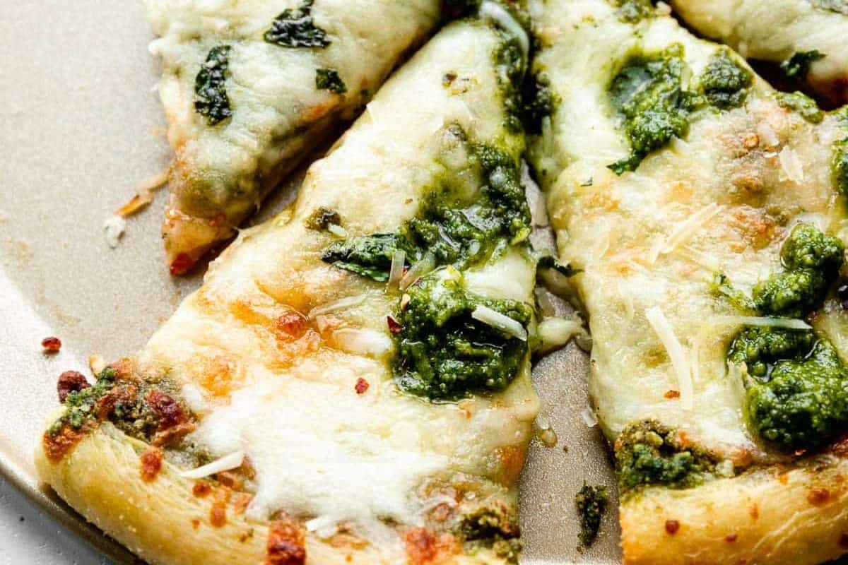 Close-up of pizza slices with melted cheese and flavorful pesto sauce on a beige plate.