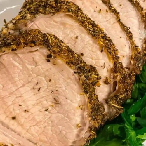 Sliced roasted pork tenderloin with seasoned crust, served on a plate with fresh parsley garnish—a must-try for fans of Pork Roast Recipes.