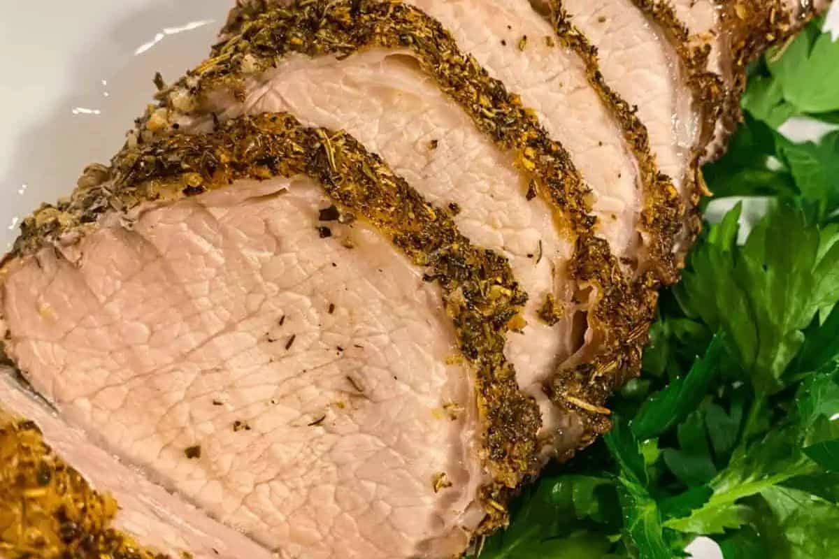 Sliced roasted pork tenderloin with seasoned crust, served on a plate with fresh parsley garnish—a must-try for fans of Pork Roast Recipes.