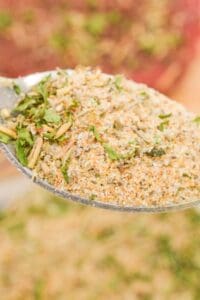A close-up of a spoon holding a blend of dried herbs and spices, including green leafy pieces and coarse powder—perfect for your homemade Pot Roast Seasoning recipe.
