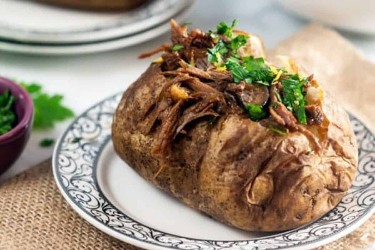 A creative baked potato topped with shredded meat and chopped fresh herbs, served on a decorative plate for a unique twist on classic baked potato recipes.