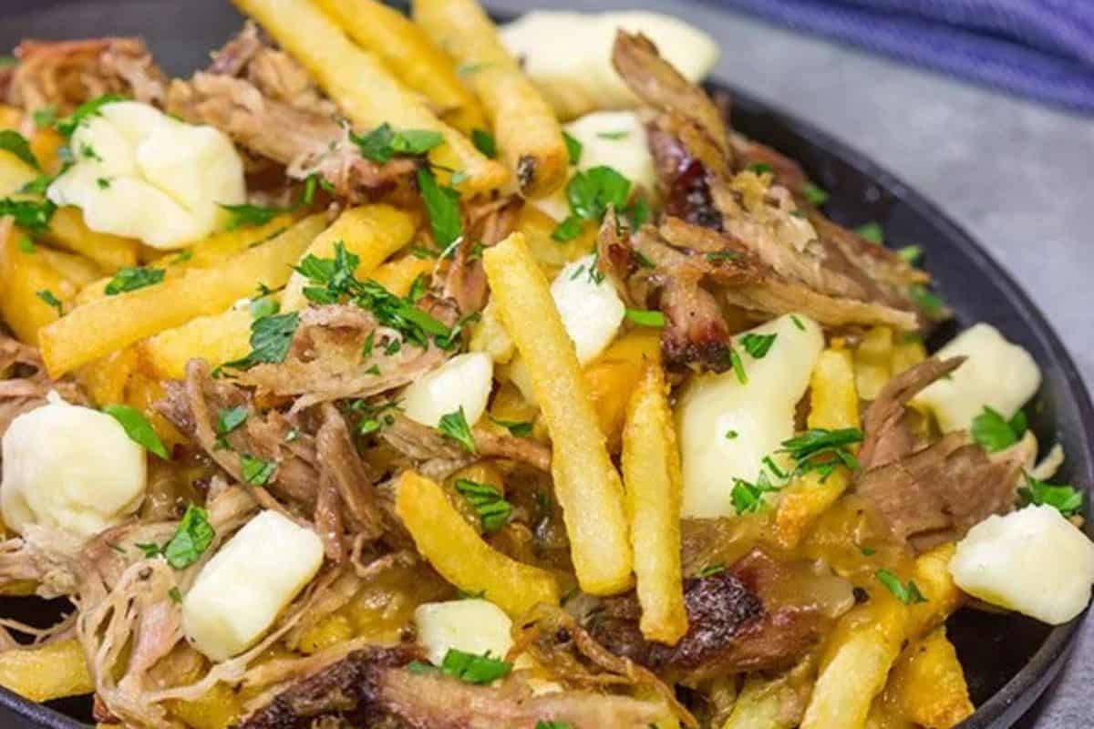 A plate of poutine topped with French fries, cheese curds, shredded meat, rich gravy, and chopped parsley delivers crazy good flavor—one of the best French fry recipes you'll ever try.
