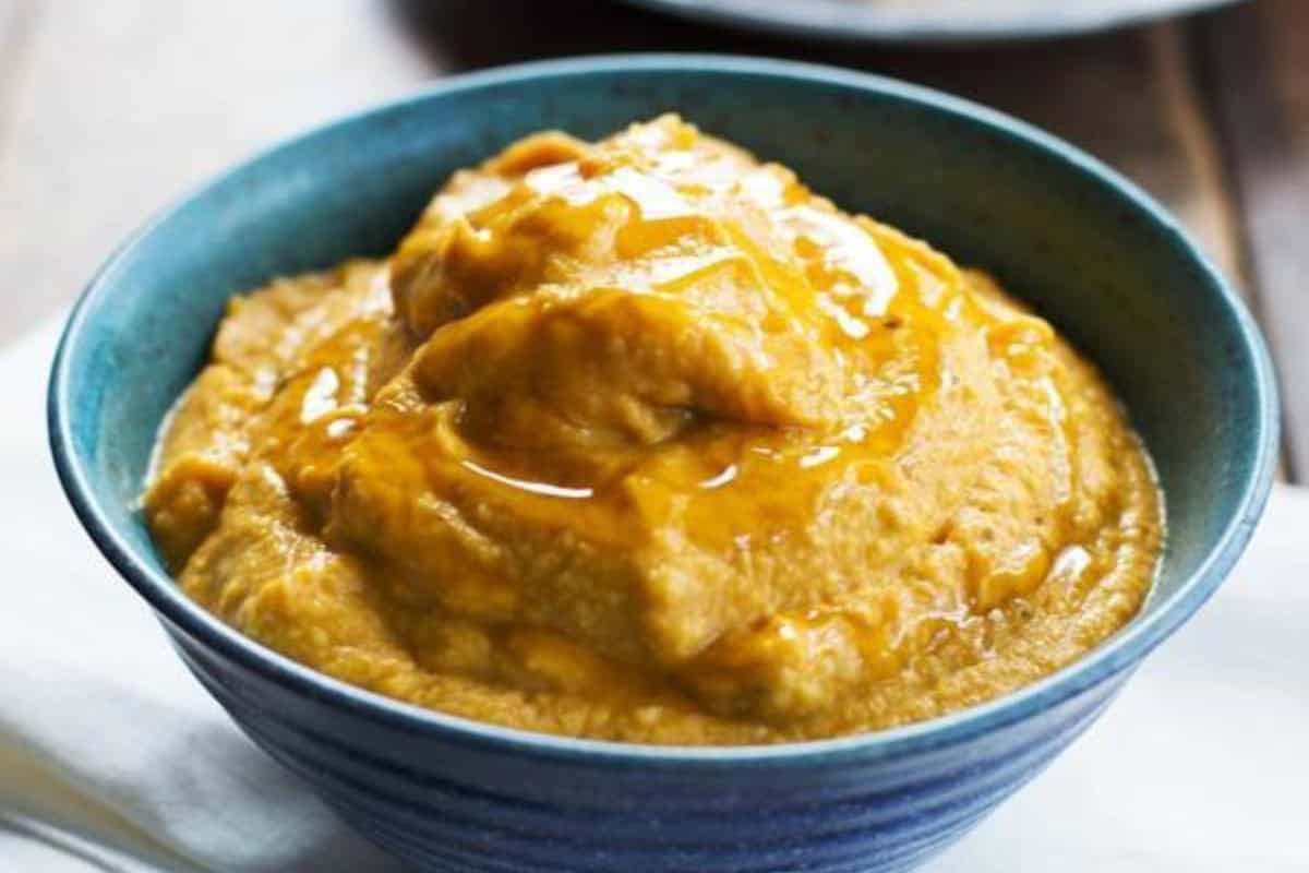 A blue bowl filled with a thick, orange-brown classic hummus puree, topped with a drizzle of golden liquid for delicious twists on tradition.