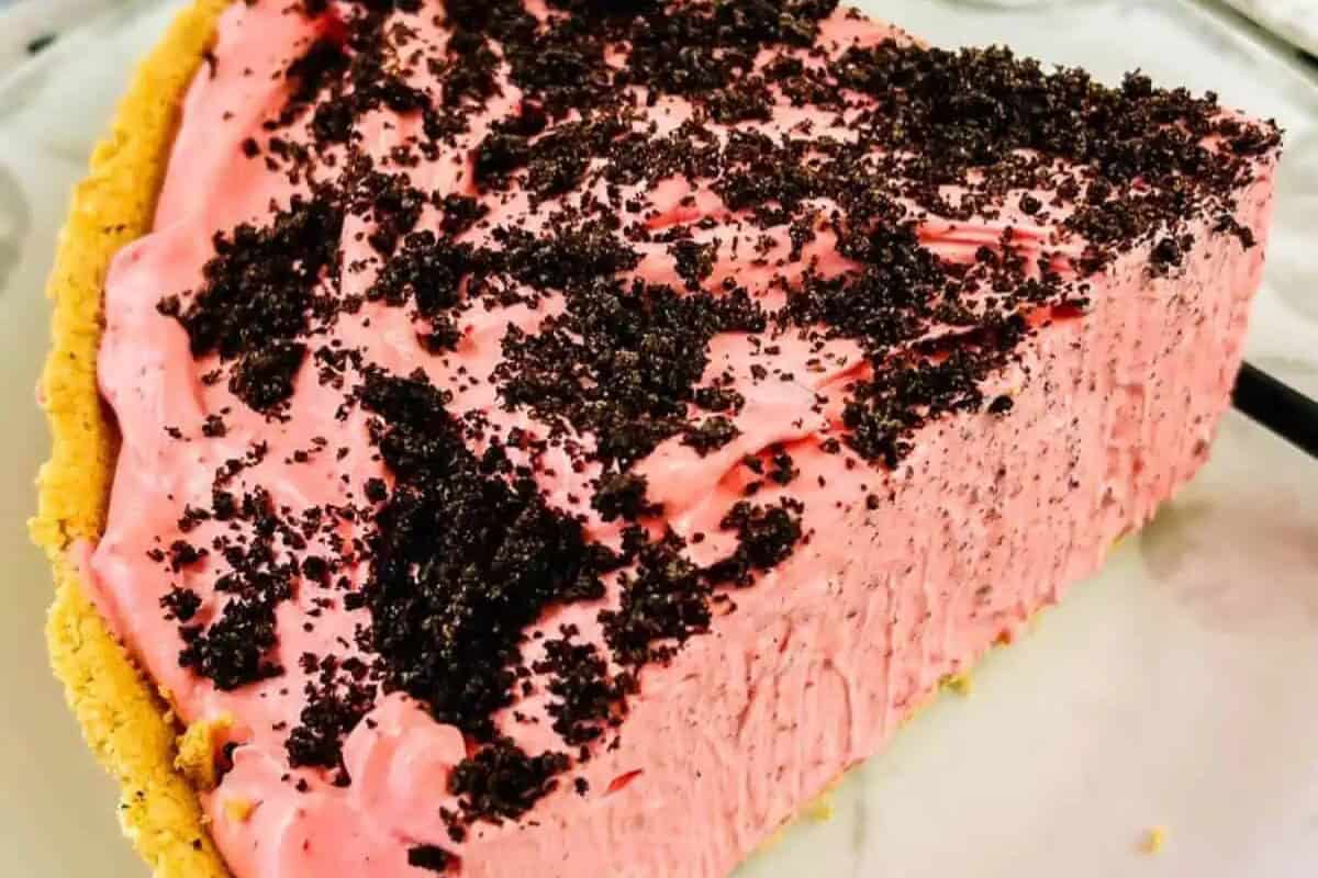A slice of pink creamy pie with a crumbly chocolate topping and a graham cracker crust on a white plate—perfect for fans of easy pie recipes or anyone seeking quick pie recipes for dessert.