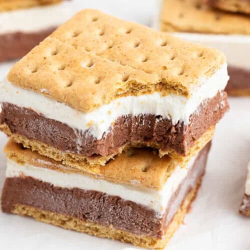 Two stacked s'mores bars with chocolate and marshmallow layers between graham crackers, with a bite taken from the top bar—an irresistible dessert perfect for summer.
