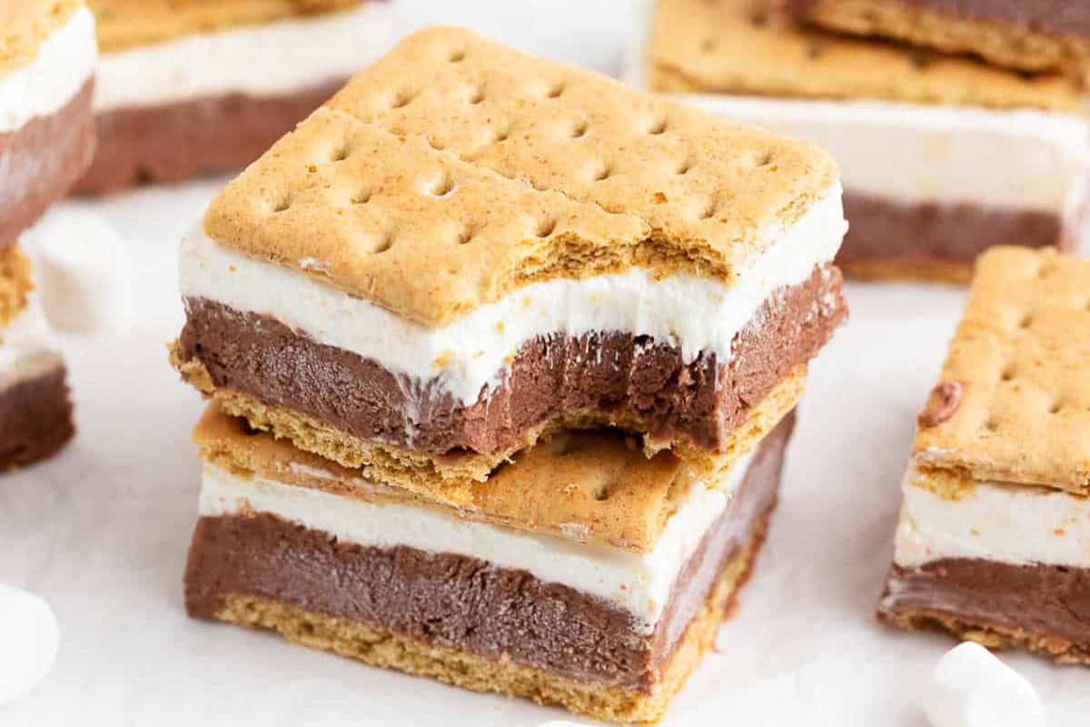 Two stacked s'mores bars with chocolate and marshmallow layers between graham crackers, with a bite taken from the top bar—an irresistible dessert perfect for summer.