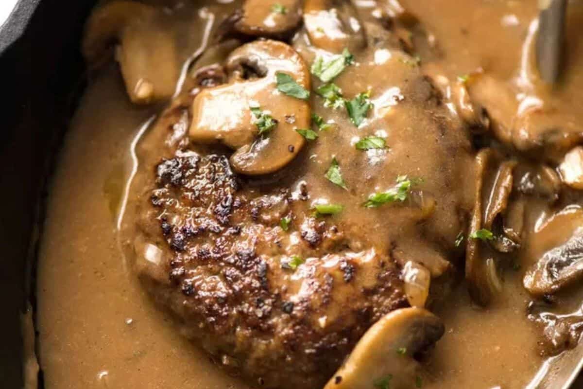 A cooked hamburger steakhouse-style, topped with brown mushroom gravy and garnished with chopped parsley.