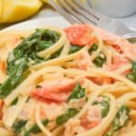 A white plate with the salmon pasta with a side of lemon slices.