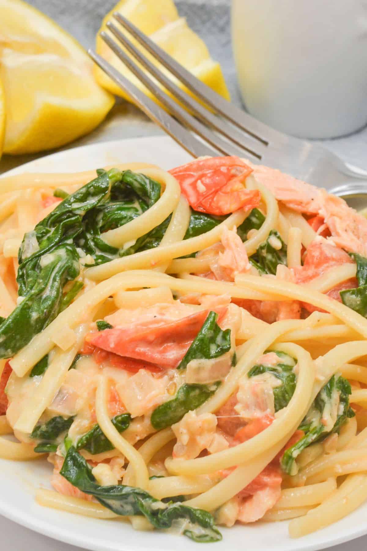 A white plate with the salmon pasta with a side of lemon slices.