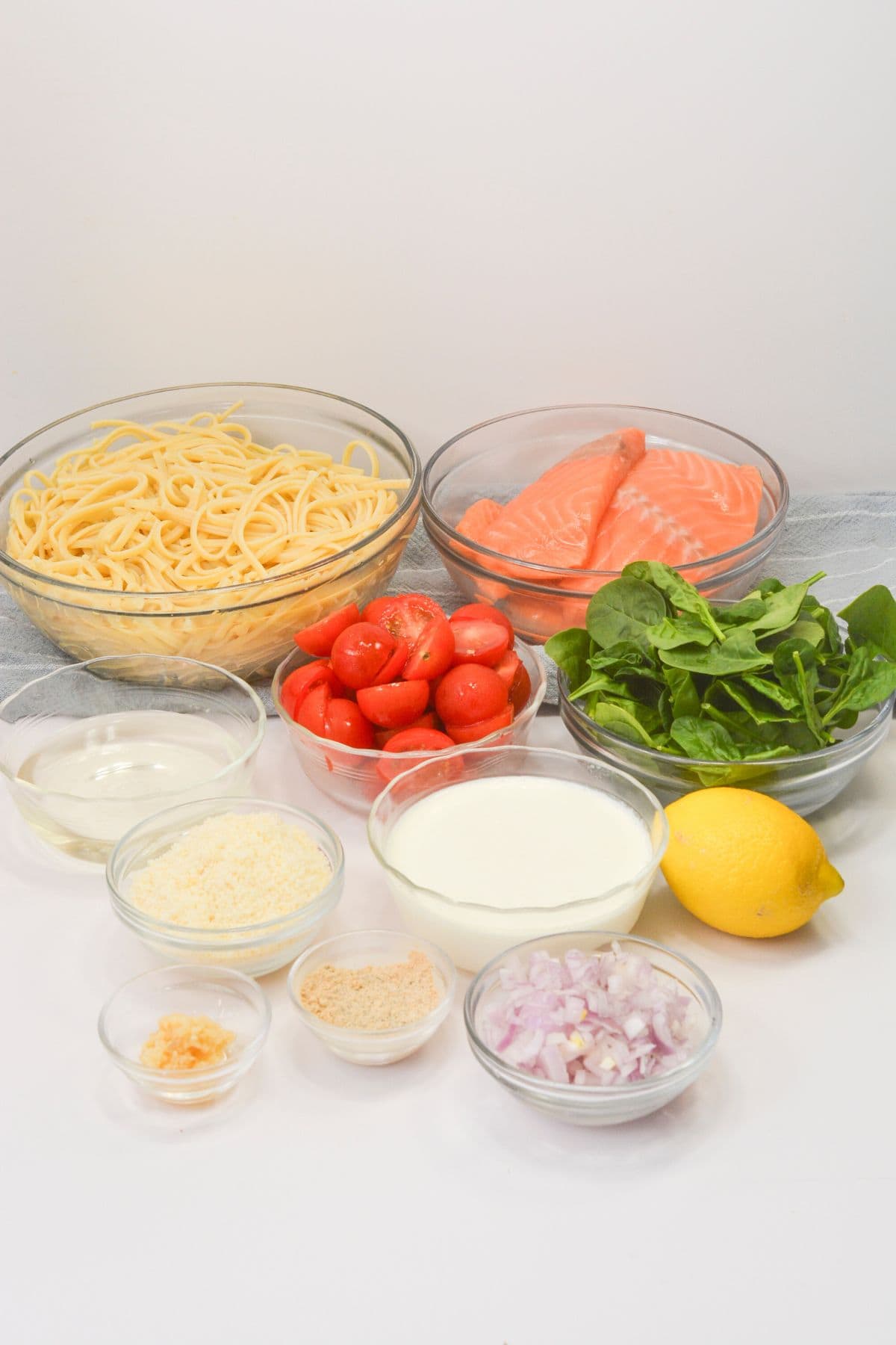 Clear glass bowls of fish, vegetables and linguini.