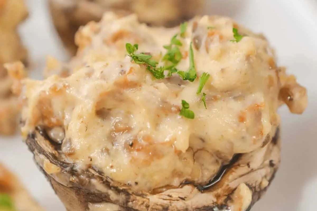 A close-up of a stuffed mushroom cap filled with a creamy mixture and topped with chopped green herbs on a white surface—a must try for anyone looking to take their Mushroom dishes beyond the basics.