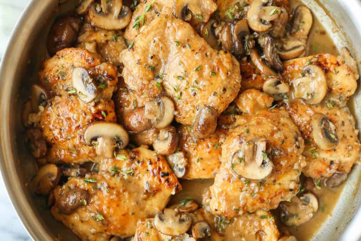 Cooked chicken thighs with sautéed mushrooms and herbs in a skillet, coated in a light brown sauce—this must try mushroom dish goes beyond the basics for savory, satisfying flavor.