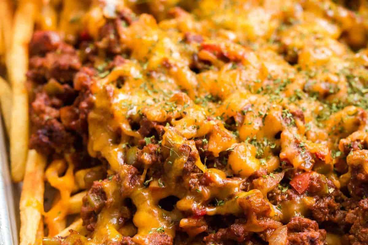 Close-up of chili cheese fries topped with seasoned ground beef, melted cheddar cheese, and sprinkled herbs—this crazy good dish is a must-try for anyone who loves bold flavor and classic French fry recipes.