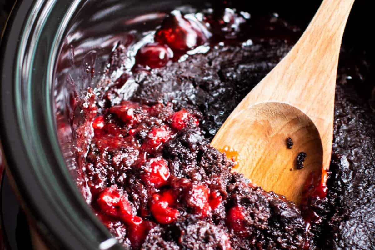 A wooden spoon scoops a mixture of chocolate cake and cherries from a slow cooker, showcasing one of the best Crock Pot Desserts for those who love effortless desserts.