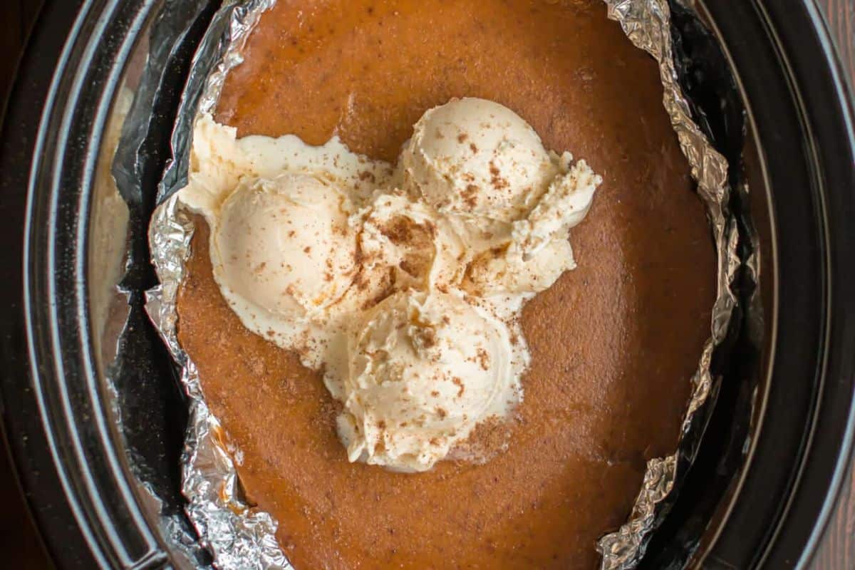 Three scoops of vanilla ice cream sprinkled with cinnamon sit on top of a pumpkin dessert in a foil-lined slow cooker—a dreamy treat for fans of Slow Cooker Desserts.