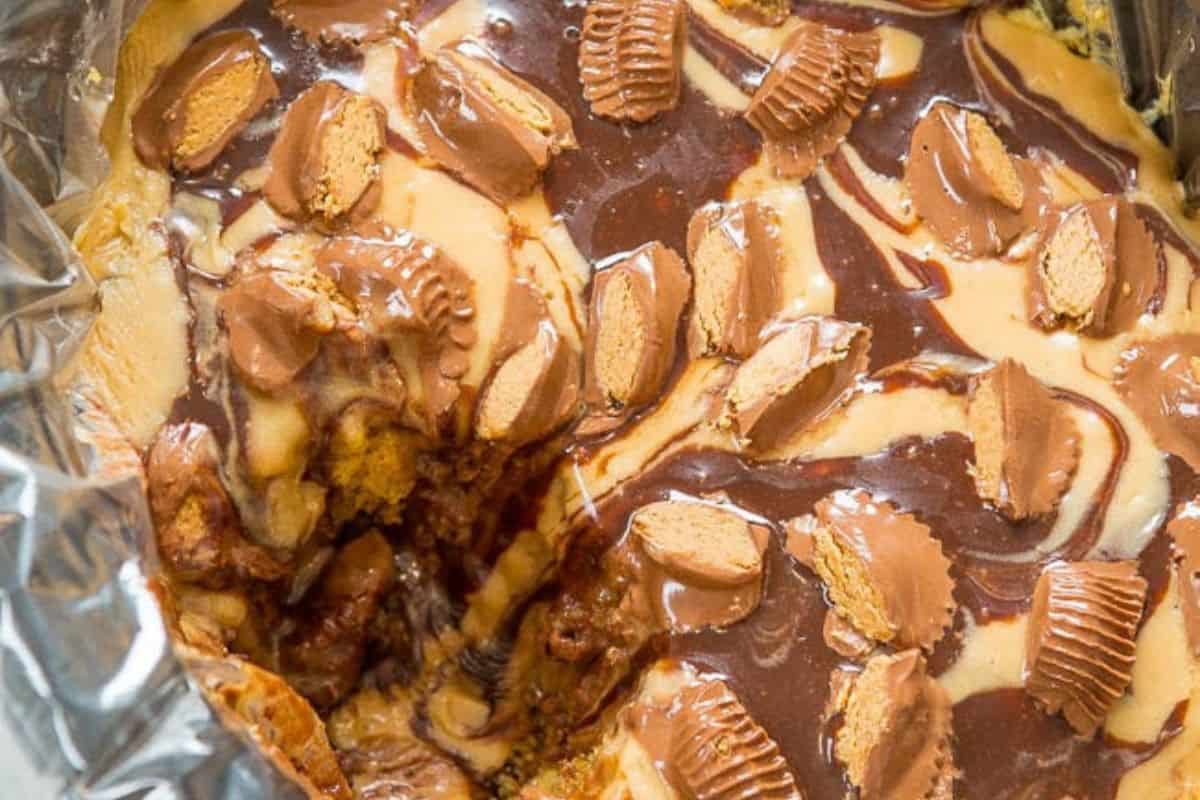 Close-up of a decadent, partially scooped dessert topped with swirls of chocolate and peanut butter, garnished with pieces of peanut butter cups—an irresistible choice for fans of effortless desserts.