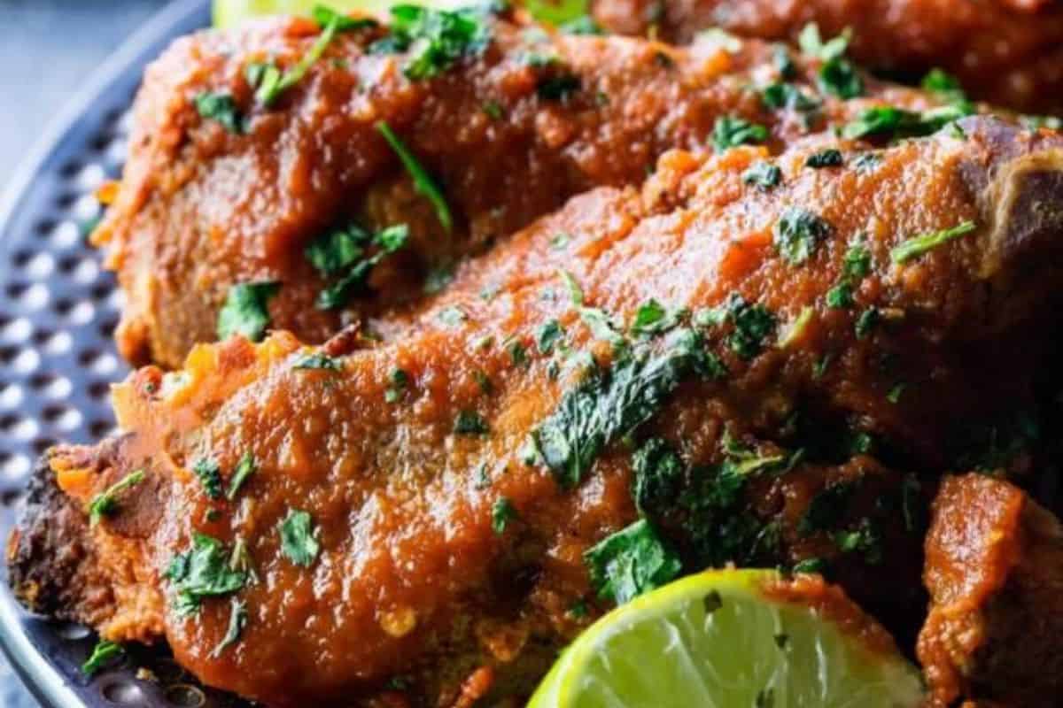 A close-up of some slow cooker pineapple chipotle ribs, served on a black plate and served next to a lime wedge.