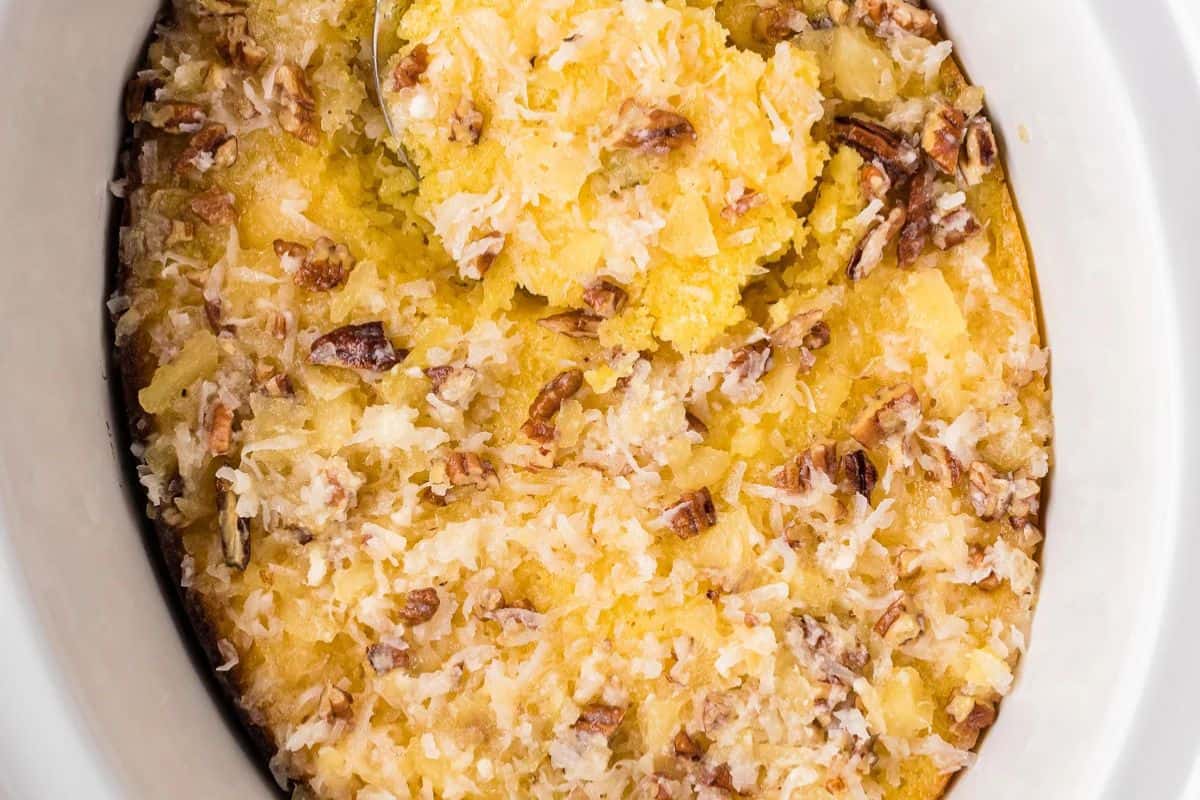 A close-up of a baked pineapple casserole topped with shredded coconut and chopped pecans in a white dish—an effortless indulgence perfect for slow cooker desserts.