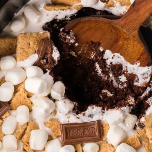 A close-up of a s'mores dessert with marshmallows, graham crackers, and chocolate bars, with a wooden spoon scooping out a portion—one of the most irresistible effortless desserts perfect for any occasion.