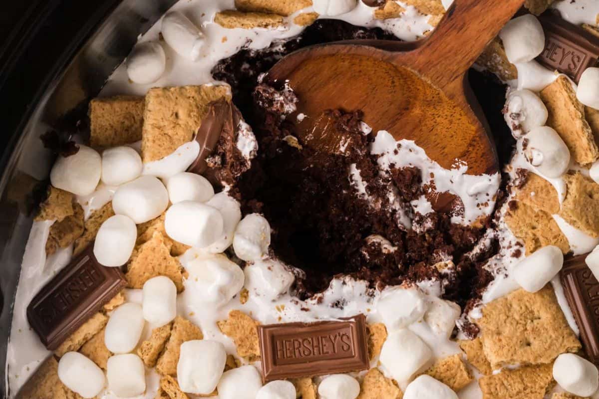 A close-up of a s'mores dessert with marshmallows, graham crackers, and chocolate bars, with a wooden spoon scooping out a portion—one of the most irresistible effortless desserts perfect for any occasion.