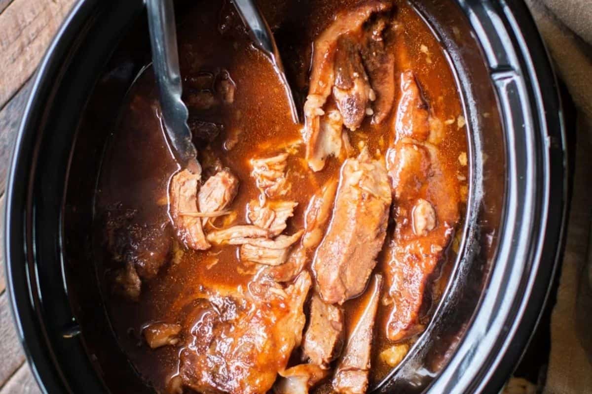 A close-up of some slow cooker sweet and sour country style ribs, pictured cooking in a crock pot slow cooker.
