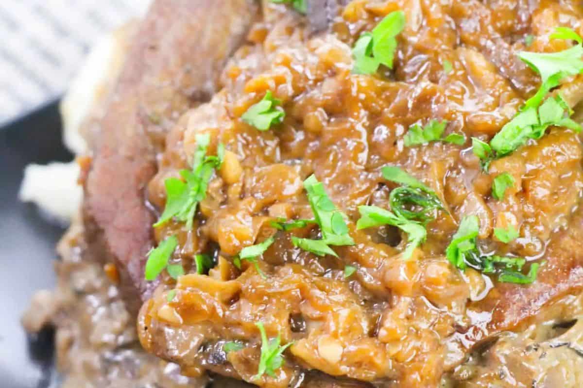 Close-up of a juicy steak dish topped with chunky brown sauce and garnished with chopped fresh herbs, perfect for fans of classic steakhouse flavors.