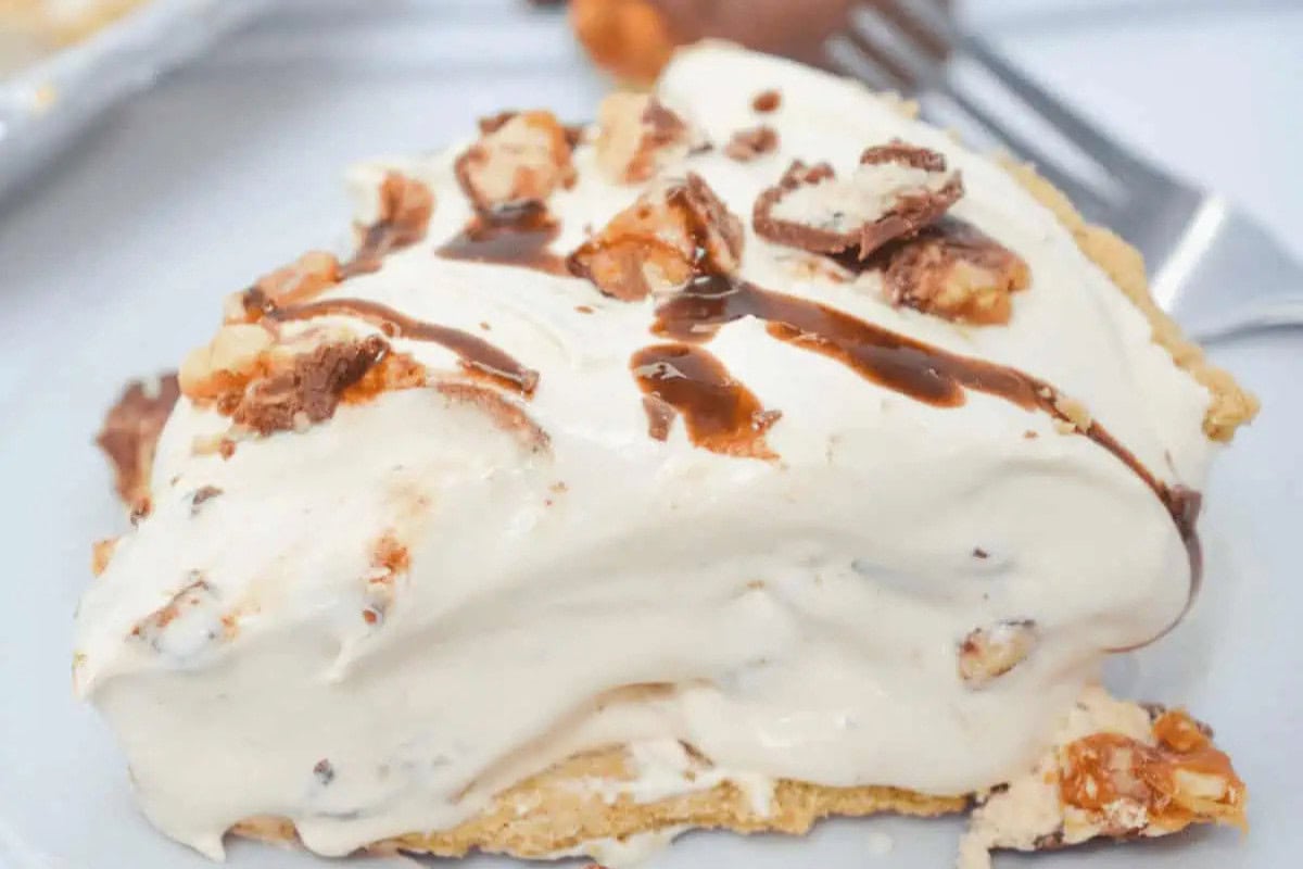 A slice of creamy pie topped with chopped nuts, chocolate pieces, and a drizzle of chocolate sauce on a white plate—perfect for fans of easy pie recipes.