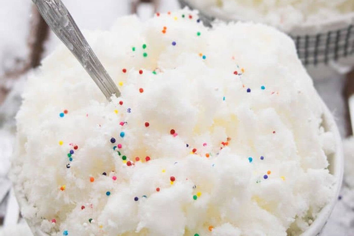 A bowl of shaved ice, one of the most irresistible frozen desserts, is topped with colorful round sprinkles and served with a spoon sticking out of the side.