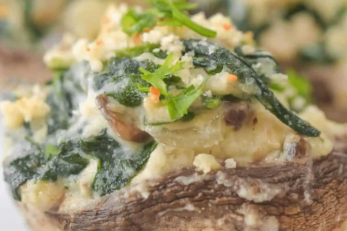 Close-up of a stuffed mushroom cap filled with a creamy spinach mixture, topped with breadcrumbs and garnished with chopped herbs—an elevated pick for those seeking mushroom dishes beyond the basics.