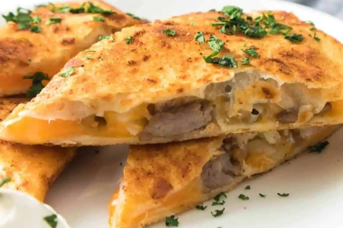 A close-up of two cheesy quesadilla slices filled with juicy steak and topped with chopped herbs, served on a white plate.