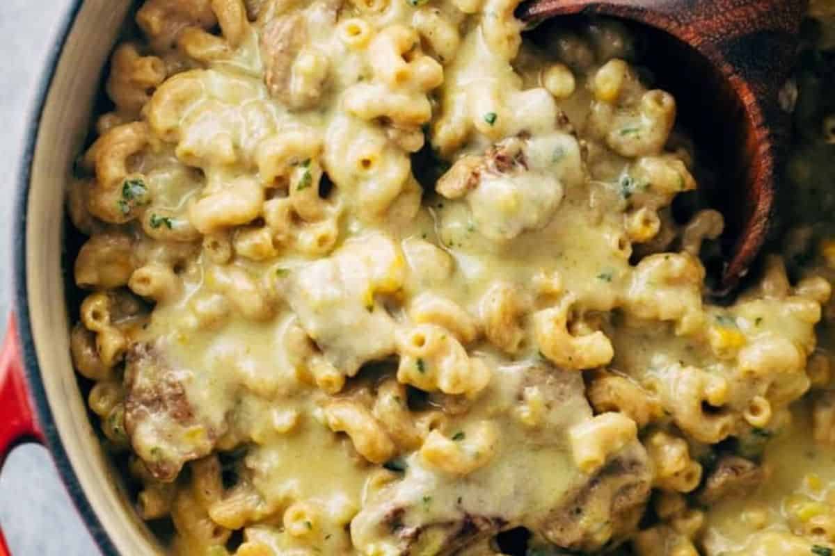 Creamy macaroni and cheese with beef pieces in a pot, reminiscent of classic steakhouse flavors, being stirred with a wooden spoon.