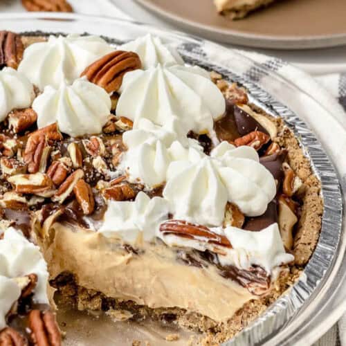 A peanut butter pie in a graham crust topped with whipped cream, pecans, and chocolate, with one slice missing—a dreamy treat perfect for fans of Easy Pie Recipes.