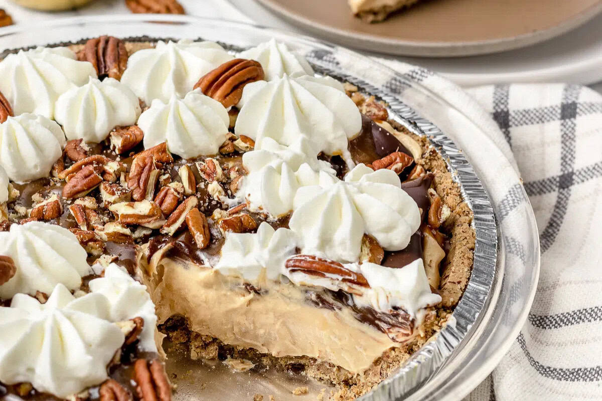 A peanut butter pie in a graham crust topped with whipped cream, pecans, and chocolate, with one slice missing—a dreamy treat perfect for fans of Easy Pie Recipes.