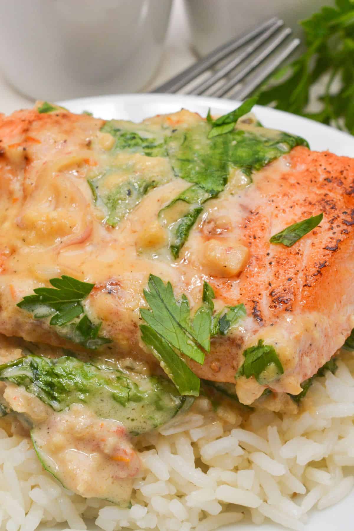 A grilled Tuscan Salmon fillet with creamy spinach sauce served on a bed of white rice, garnished with fresh parsley.