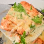 A close-up of a creamy, herb-covered cooked chicken breast being lifted from a pan with a spatula, echoing the rich flavors and textures of Tuscan Salmon.