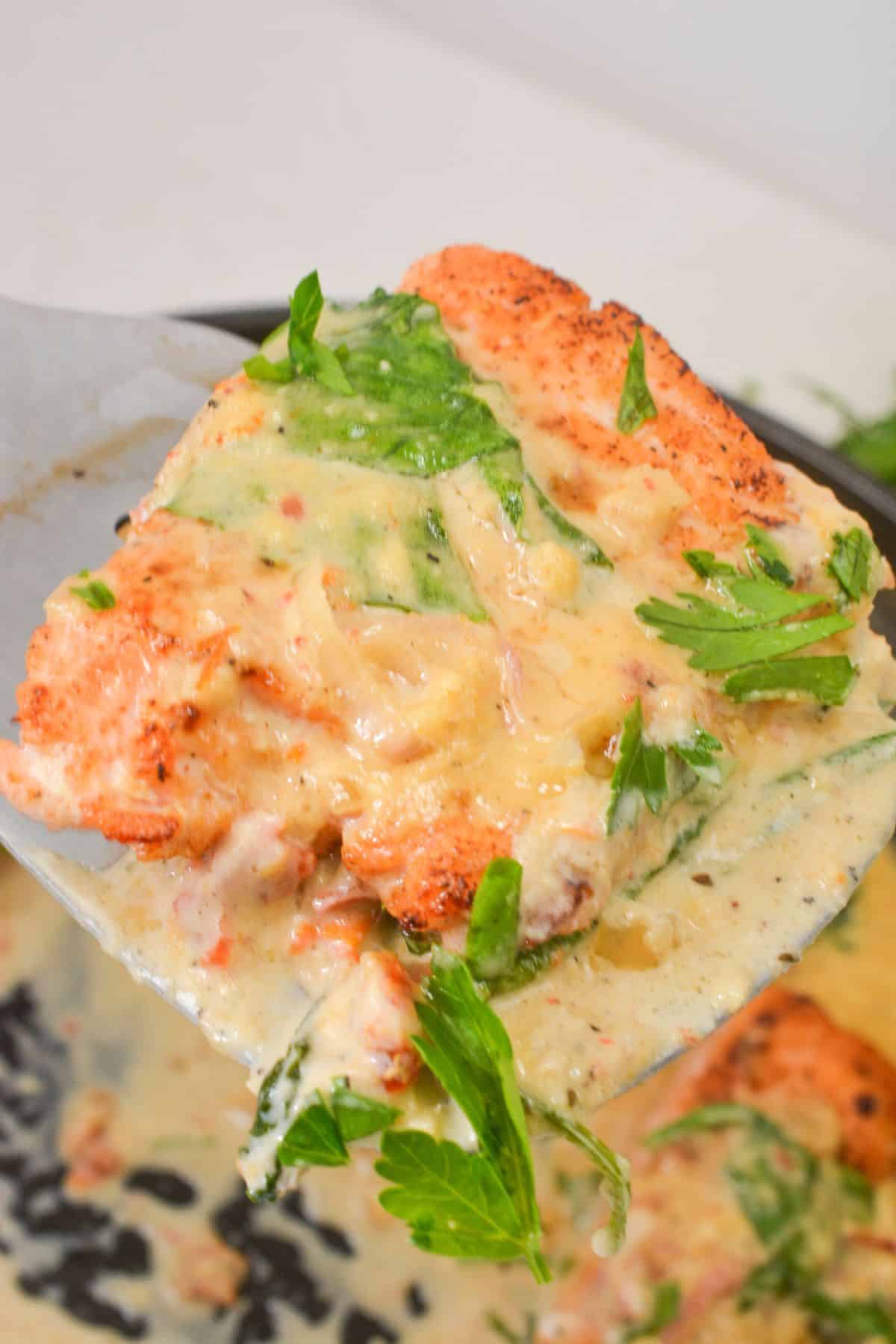 A close-up of a creamy, herb-covered cooked chicken breast being lifted from a pan with a spatula, echoing the rich flavors and textures of Tuscan Salmon.