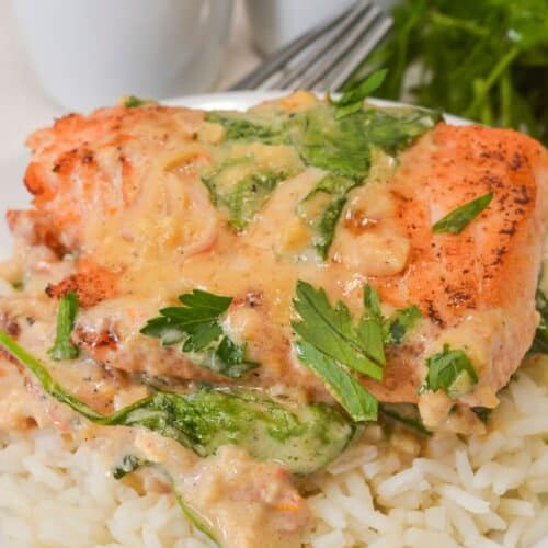 A piece of Tuscan Salmon topped with creamy spinach sauce served over white rice, garnished with parsley, with salt and pepper shakers in the background.