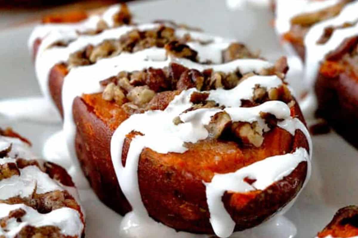 A halved baked sweet potato topped with chopped nuts and drizzled with white icing on a white plate—an irresistible twist for anyone looking for new baked potato ideas.
