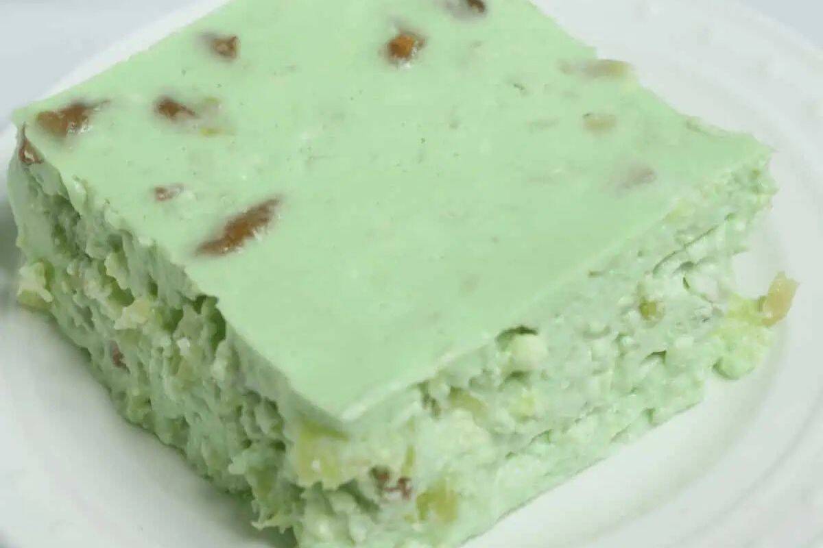 Close-up of a slice of green lime cottage cheese jello salad, served on a white plate.
