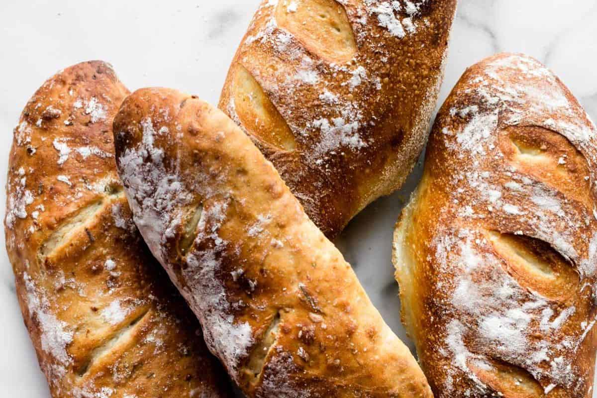 Four loaves of rustic bread with golden, crispy crusts and dusted with flour, arranged on a white surface—perfect quick breads you can bake anytime.