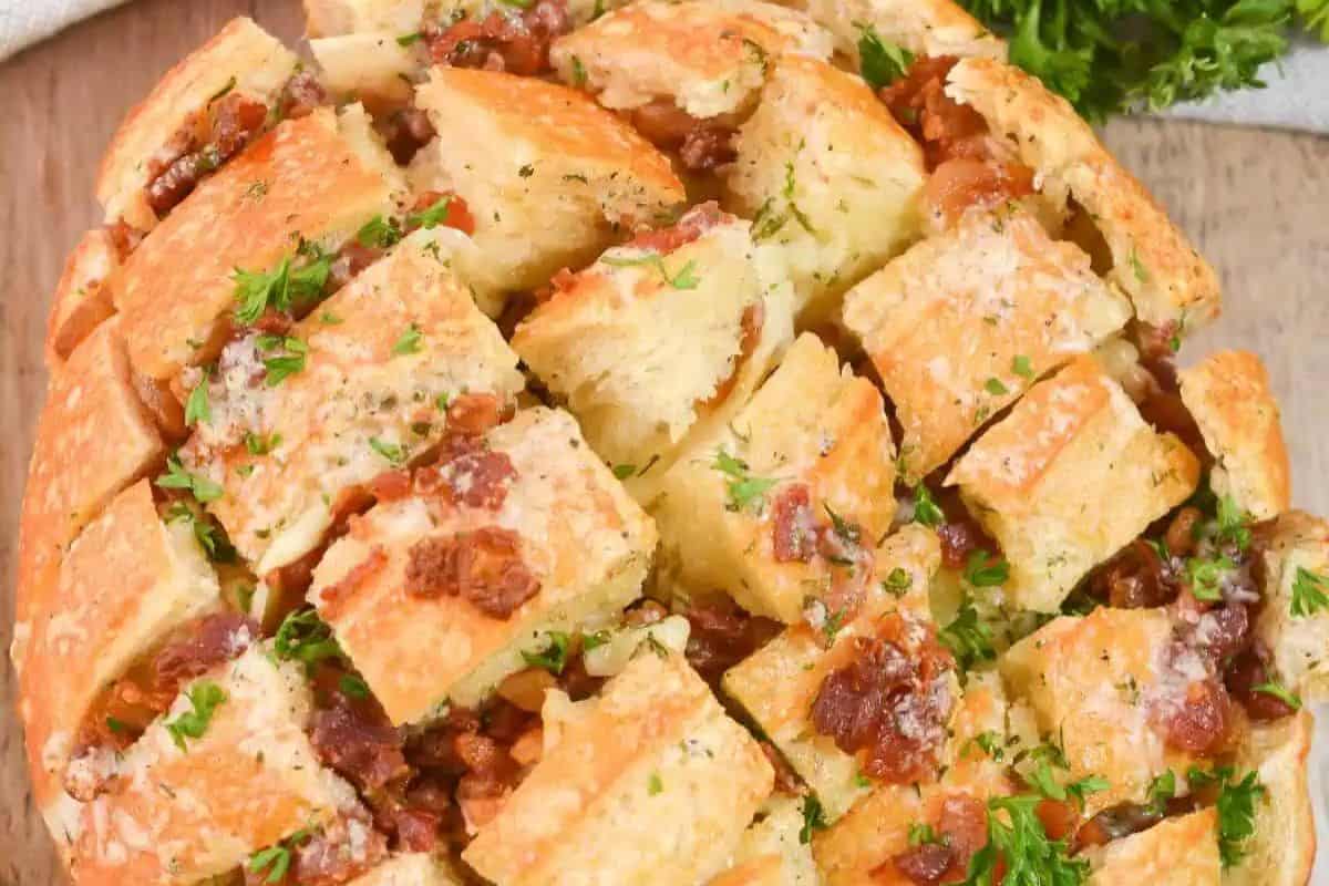 A round loaf of bread sliced in a crisscross pattern, filled with bacon, herbs, and melted cheese—this easy bake is perfect for anytime you crave delicious quick breads.