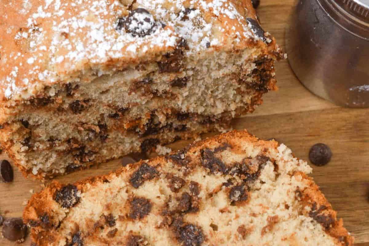 A close-up of a sliced loaf of chocolate chip bread on a wooden surface, sprinkled with chocolate chips and powdered sugar—a must try for anyone who loves quick breads and wants to bake anytime.