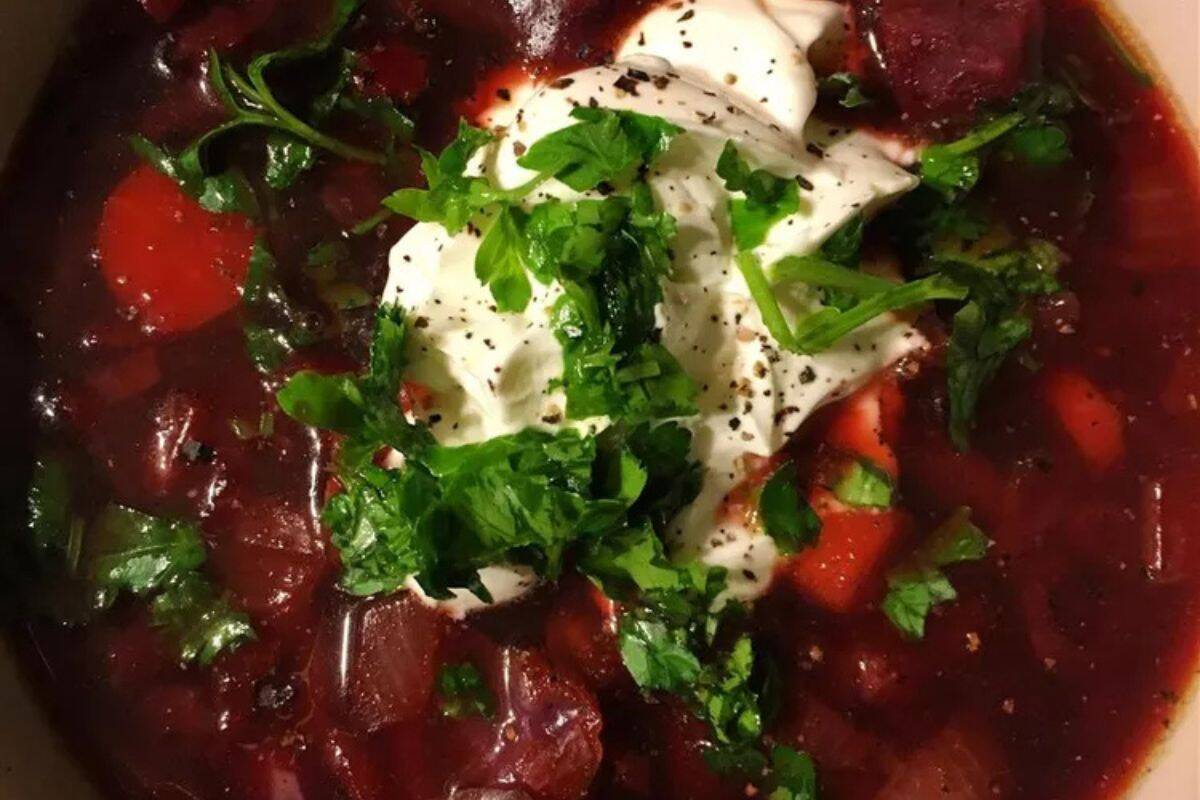 Hearty bowl of beef and beet borscht soup garnished with fresh herbs and a dollop of sour cream.