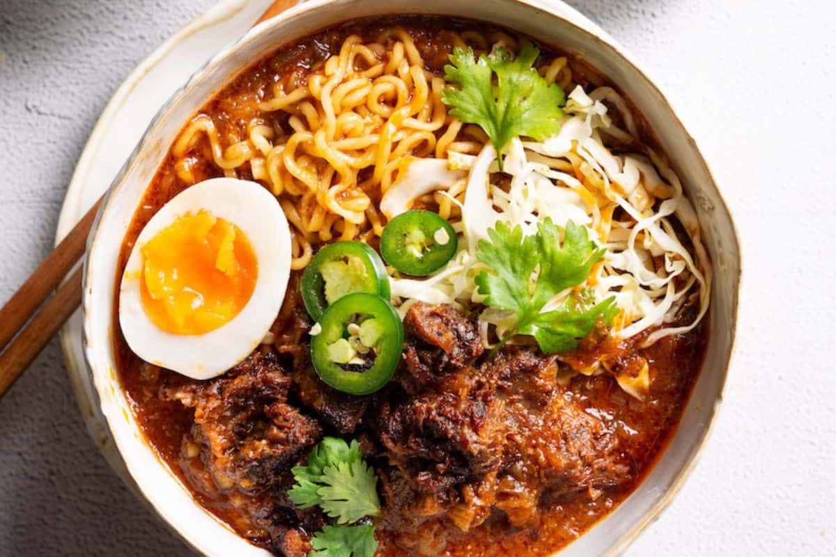 A bowl of flavor packed ramen topped with braised meat, shredded cabbage, sliced jalapenos, half a soft-boiled egg, and fresh cilantro.
