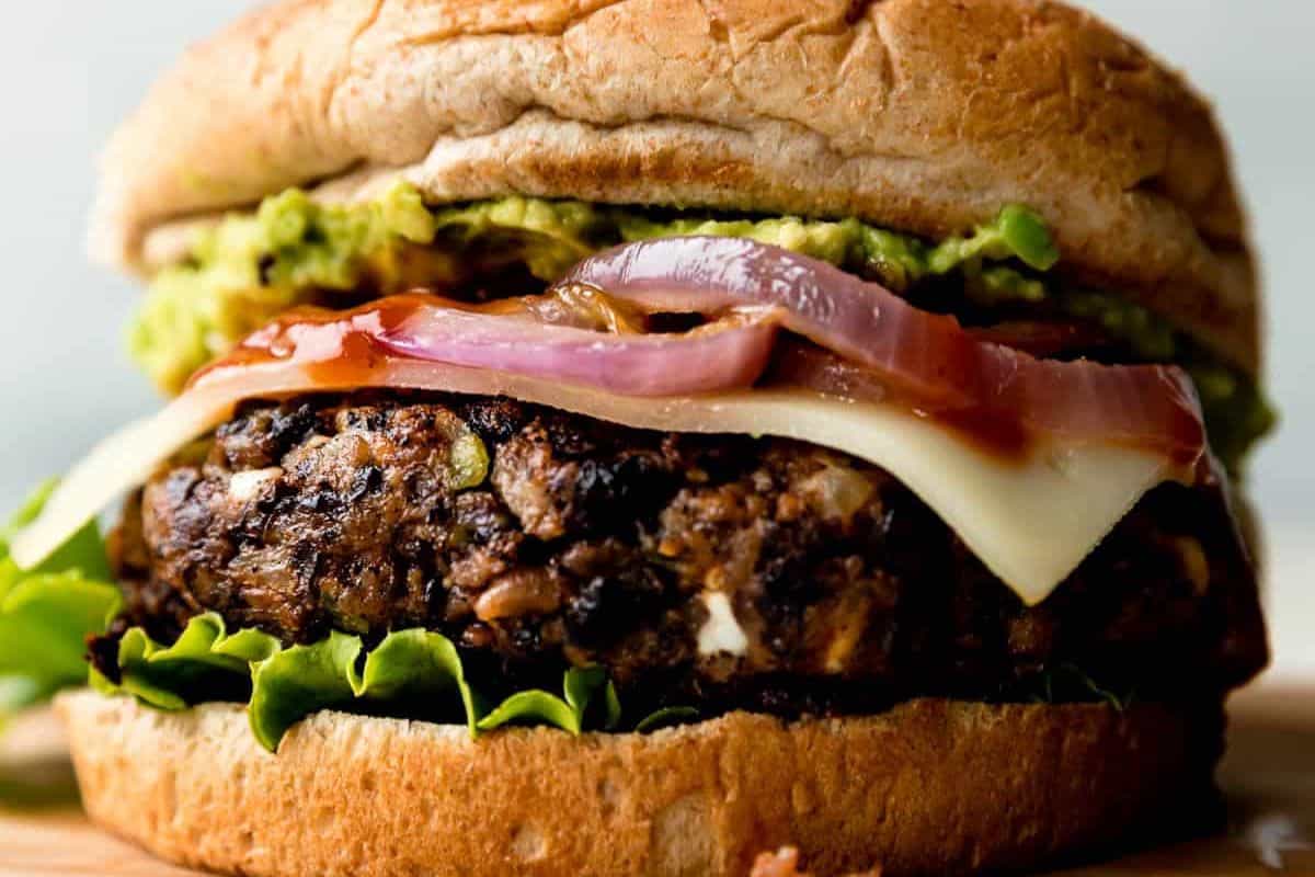 Close-up of a veggie burger with a whole wheat bun, leafy lettuce, a patty made with canned beans, melted cheese, grilled onions, and guacamole—one of those easy recipes that turns into truly delicious dishes.
