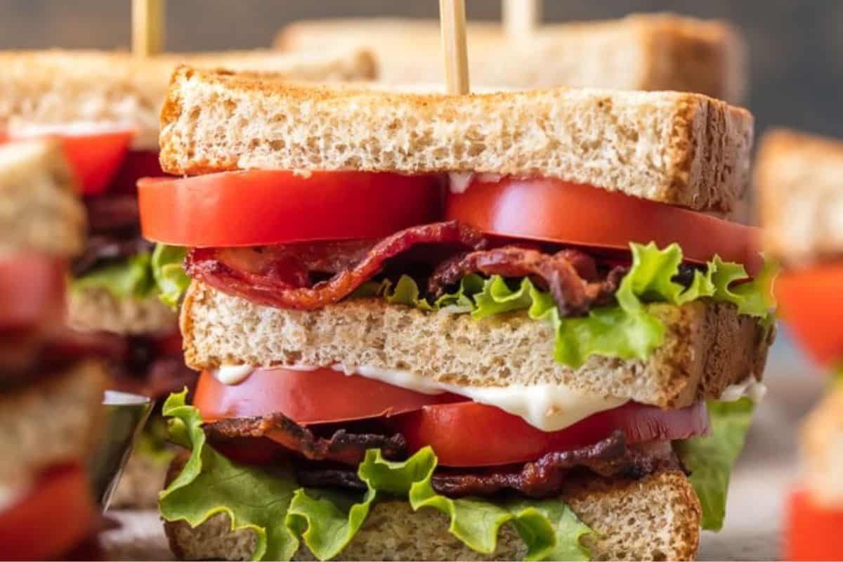 A close-up of a classic BLT—one of the most delicious sandwiches—with layers of bacon, lettuce, tomato, mayonnaise, and toasted bread, held together with a wooden skewer.